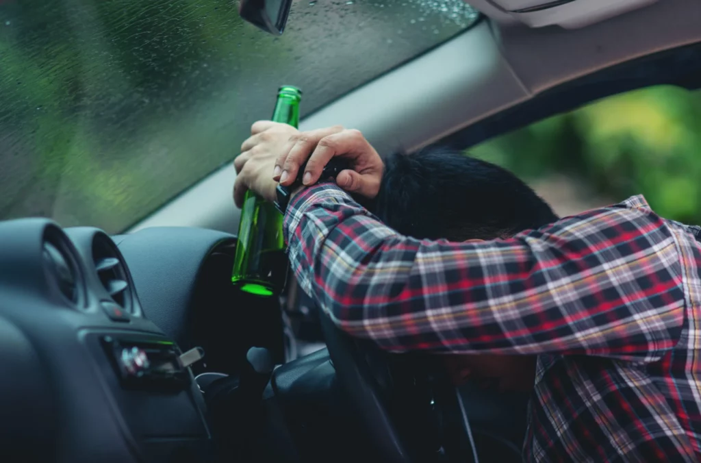 man holds a beer bottle while is driving a car